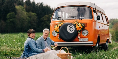 Hochzeitsauto-Vermietung - Marke: Volkswagen - Frieswil - Brautpaar Picknick vor orangem VW-Bus - VW-Busse T1 & T2, Photobus, Hochzeitsauto (vwbusbern.ch)